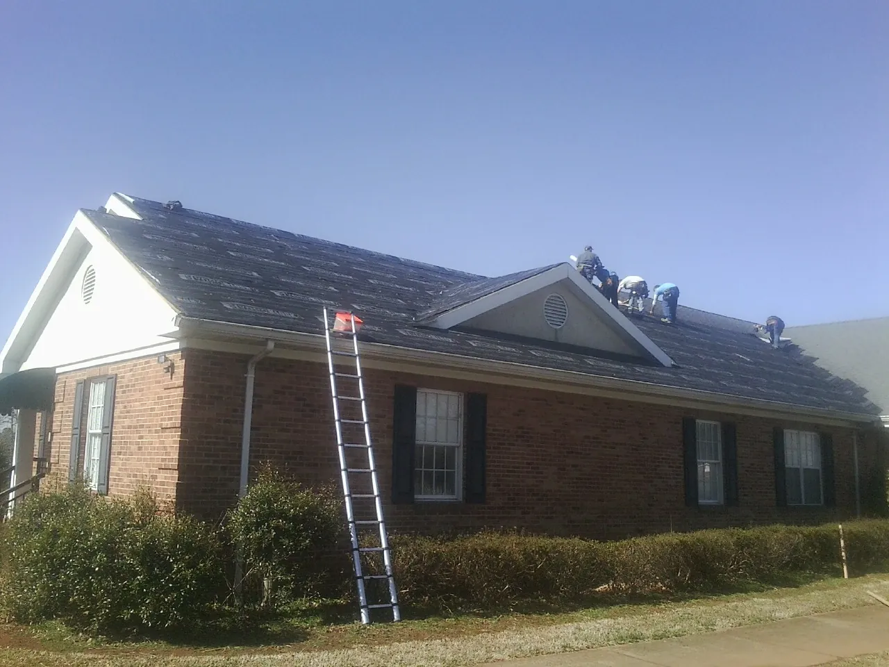 Crew tearing shingles off a brick ranch roof with a ladder set — Metal Roof Repair work by our crew in Dublin