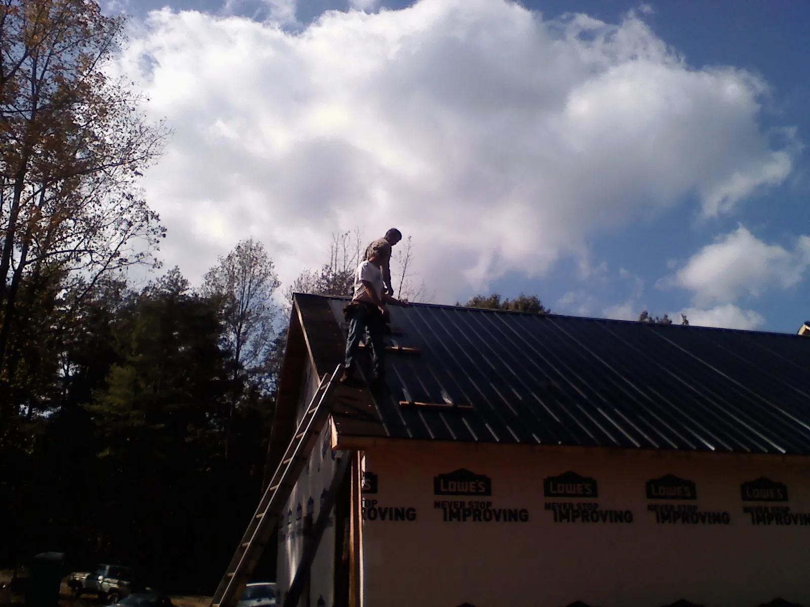 Roofer fastening dark metal panels high against a cloudy sky, from a Roof Inspection job in Dublin