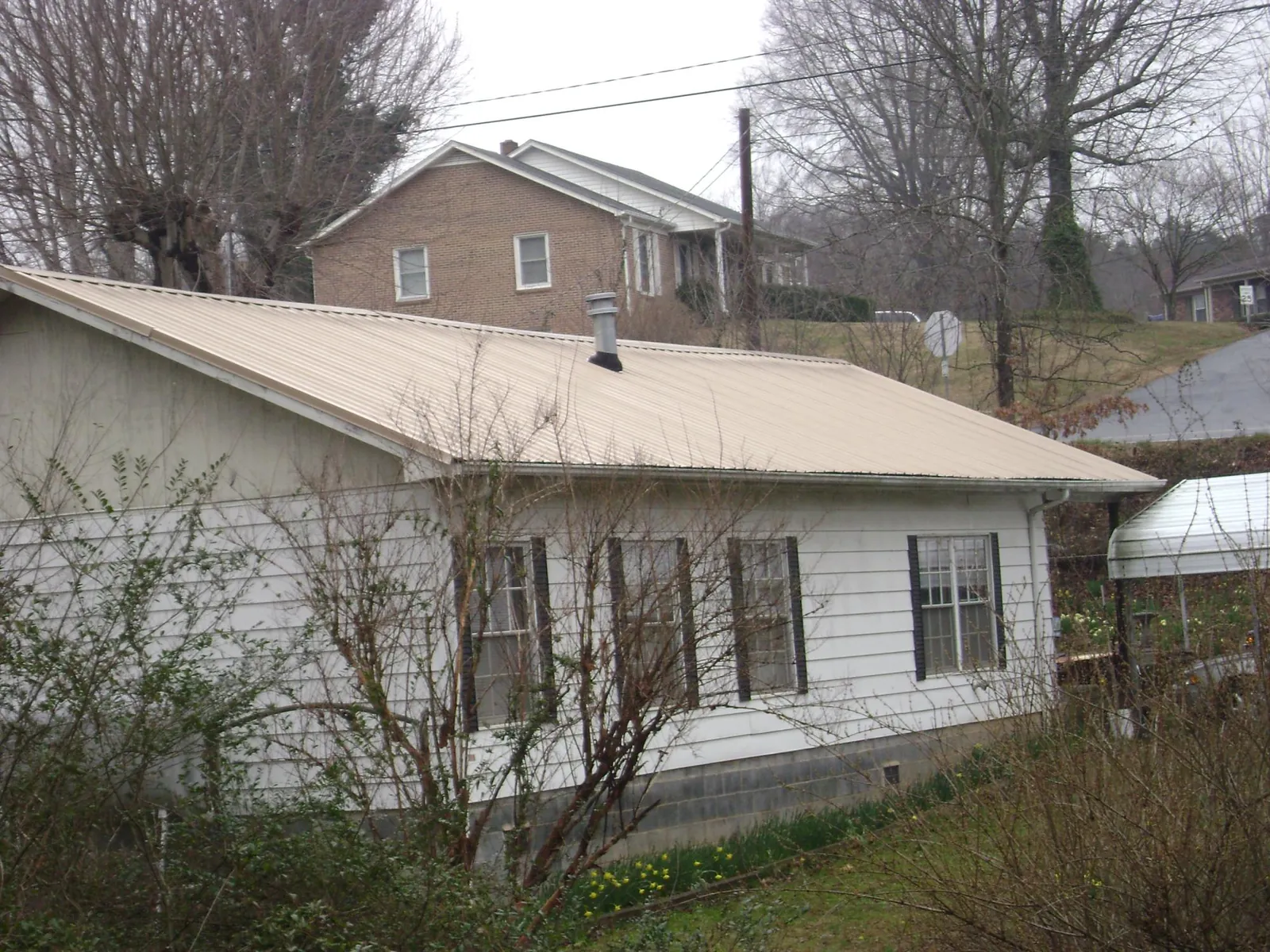Tan metal roof on a white sided house set into a hillside — Commercial Roofing by Roofing Brothers in Dublin